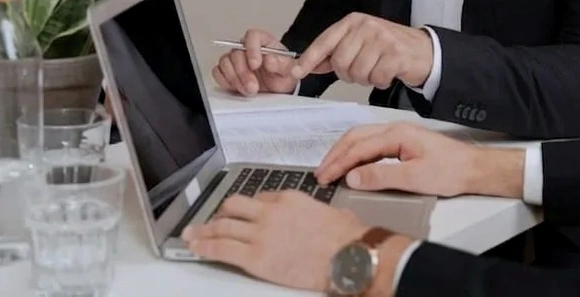 Detalle de una reunión de trabajo: manos, documentación y computadora